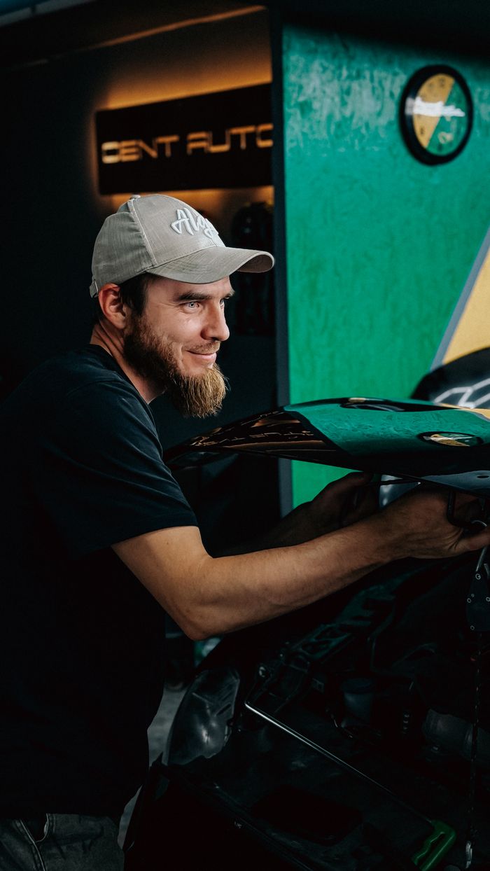 Smiling auto technician working on a vehicle in a modern garage setting.